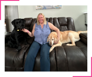 Kim on sofa with two Seeing eye dogs. Retired Yellow lab, Vicar on left. Working black lab, Reba on right.